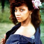 Color pic of woman shot on location with flower in hair and denim jacket off shoulder